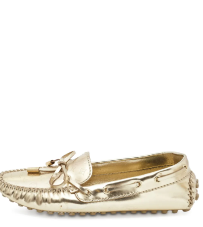 Luxurious gold-tone leather slip-on loafers crafted with a smooth metallic finish, featuring a debossed monogram pattern, elegant bow detail, signature logo appliqué, classic moc stitching, a cushioned branded leather insole, and a durable segmented rubbe
